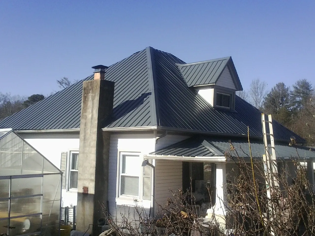 Dark blue standing seam metal roof on a white farmhouse with dormer — Slate & Tile Roof Repair by Roofing Brothers in Fort Madison