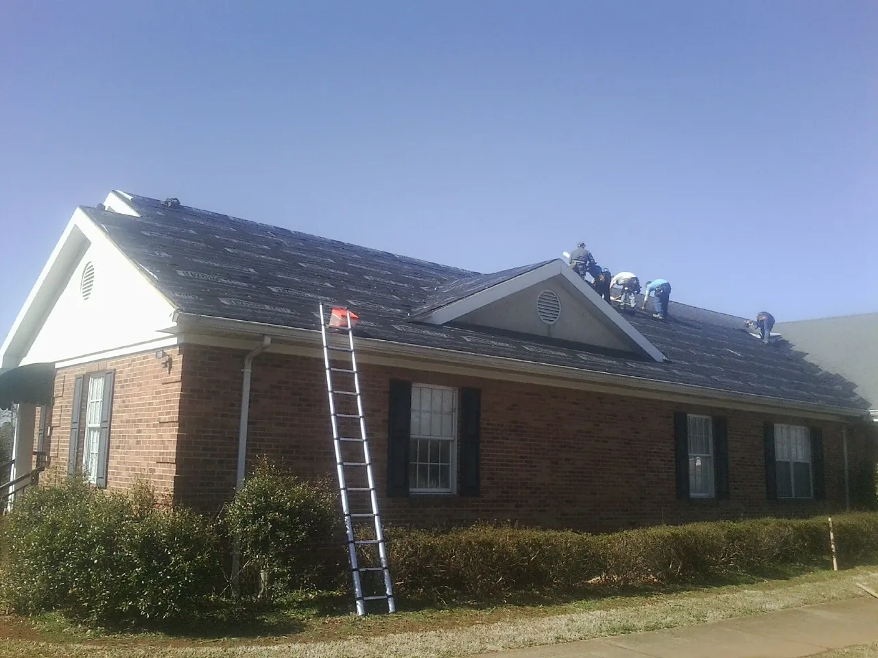 Crew tearing shingles off a brick ranch roof with a ladder set — Emergency Roof Repair work by our crew in Fort Madison