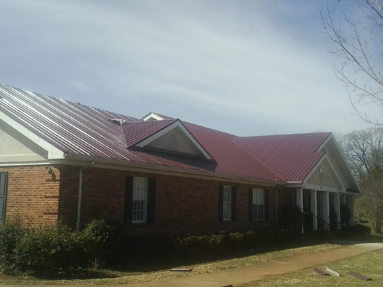 Red metal roof with gabled entries on a long brick building, from a Hail Damage Roof Repair job in Fort Madison