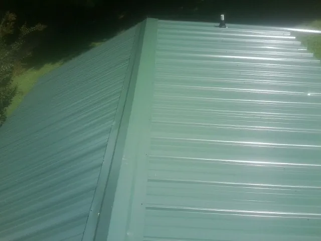 New green metal panels meeting at the ridge of a roof — Flat Roof Repair work by our crew in Fort Madison
