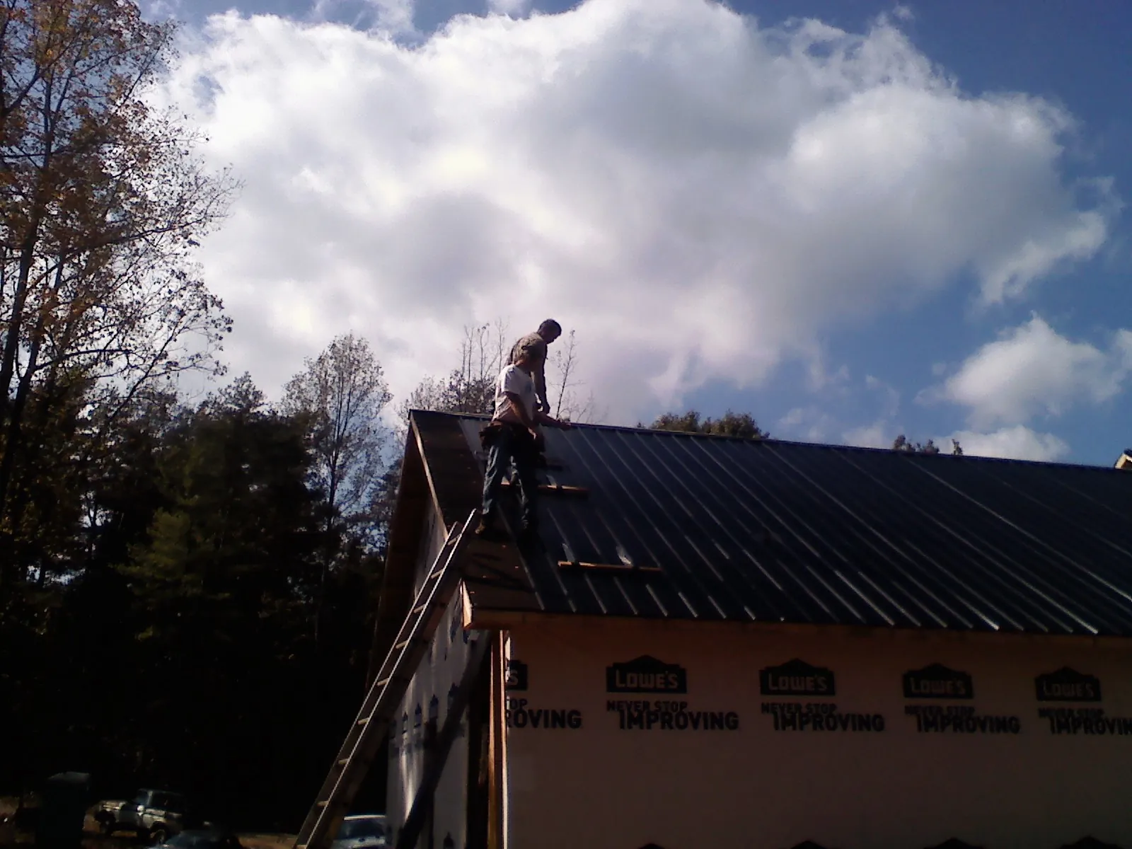 Roofer fastening dark metal panels high against a cloudy sky, from a Roof Inspection job in Fort Madison