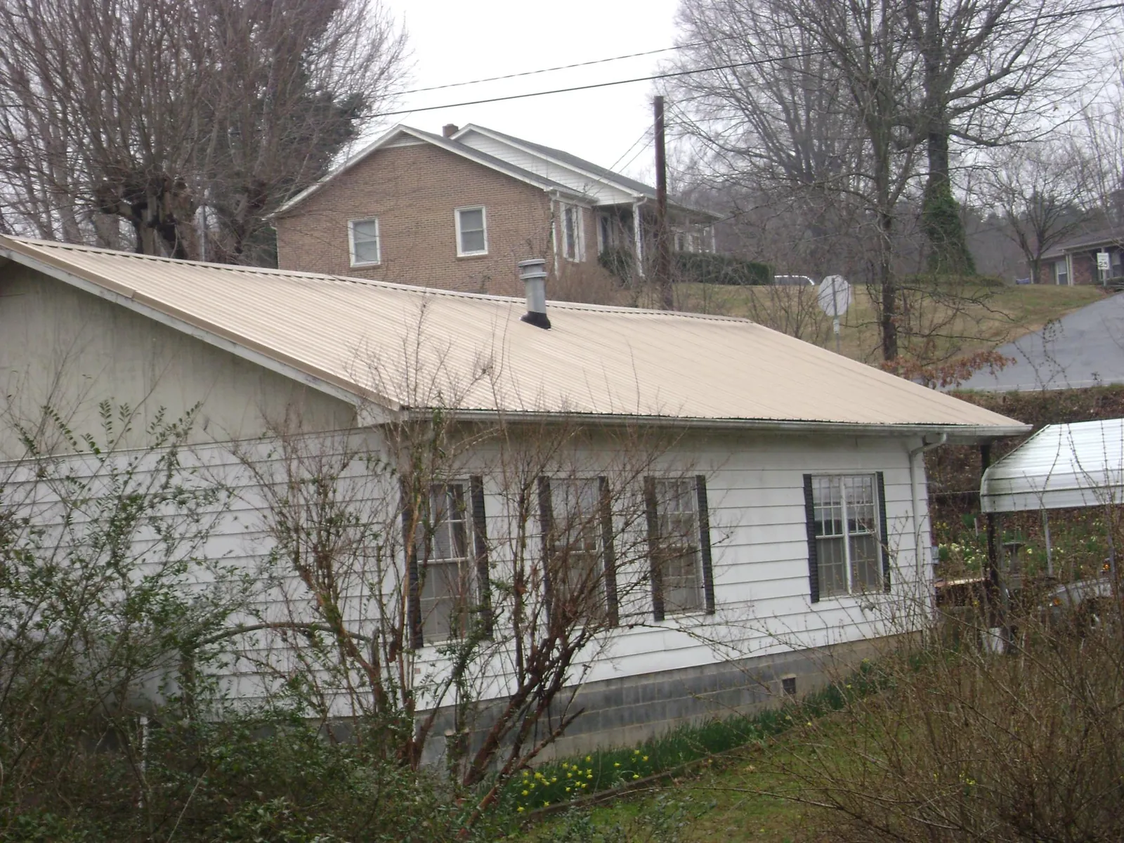 Tan metal roof on a white sided house set into a hillside — Commercial Roofing by Roofing Brothers in Fort Madison