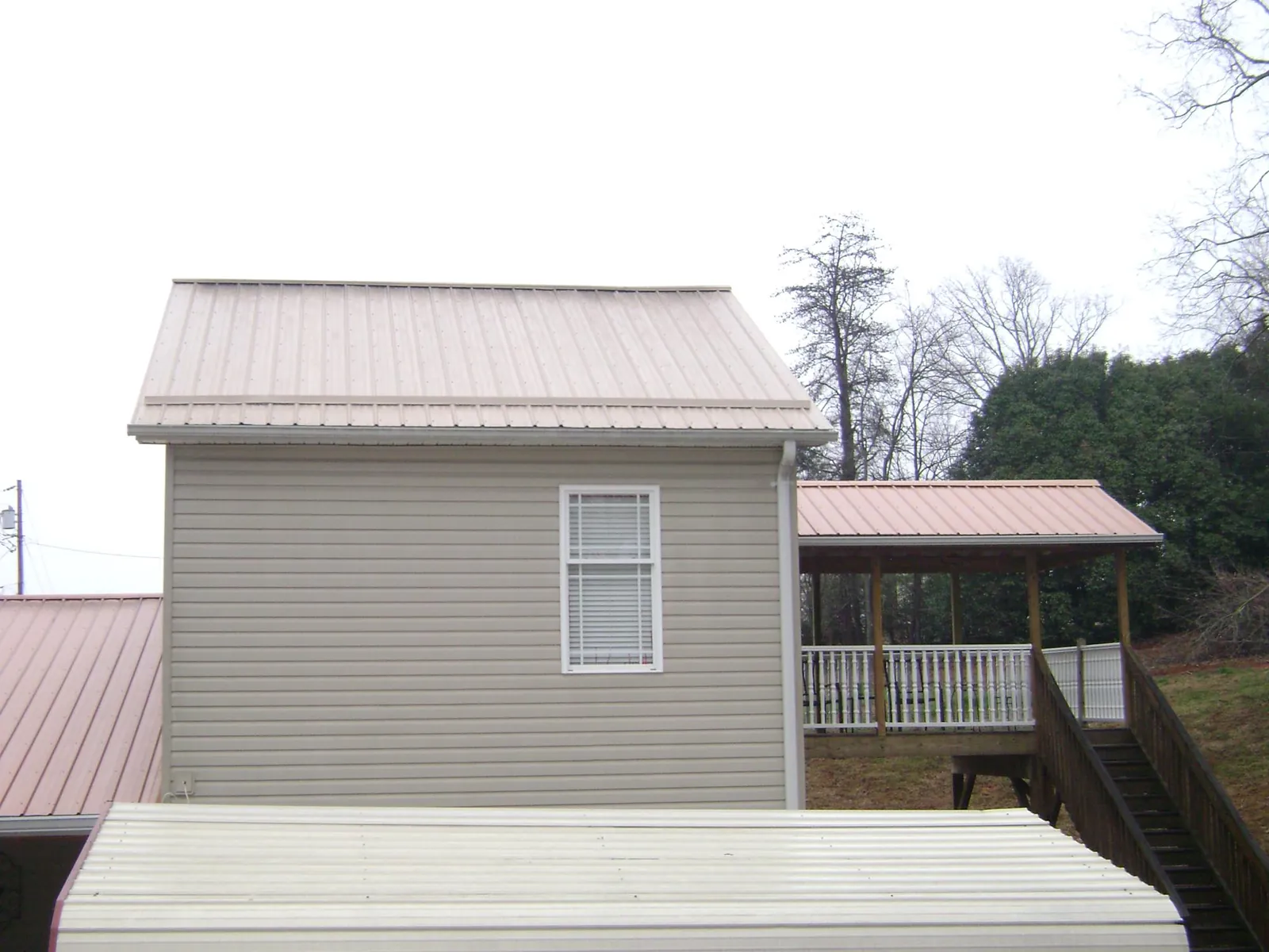 Tan metal roofs on a two story addition and attached porch, from a Roof Replacement job in Fort Madison